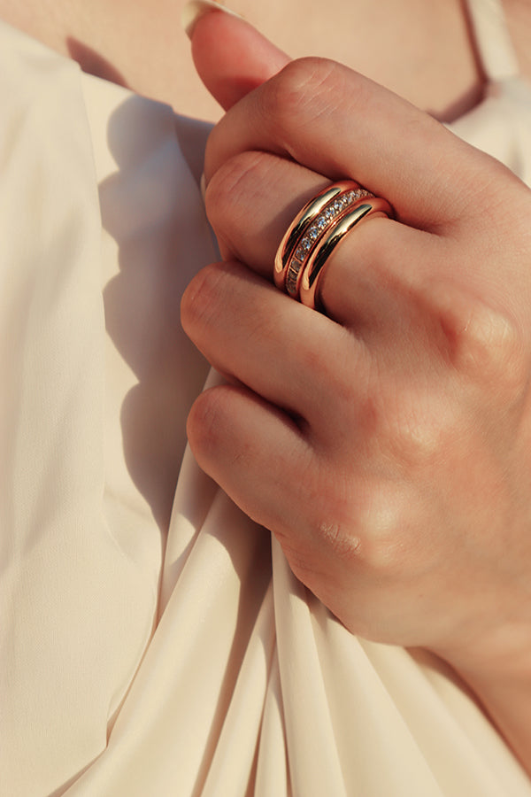 一位模特兒配戴三件經典疊戴戒指,將精緻的鋯石戒指與簡約素圈戒指層次搭配,展現優雅品味。