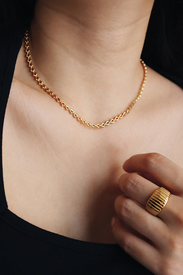 Woman in black top wearing chic gold necklace and bold statement ring.