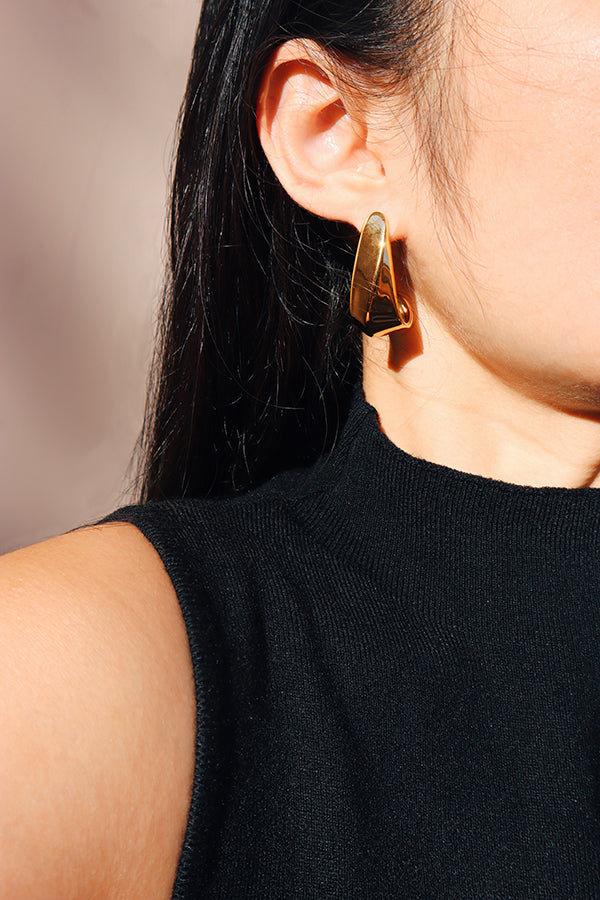 一位女性佩戴著大膽幾何金色耳環,設計簡約現代,搭配無袖黑色上衣,展現出極簡卻亮眼的風格。