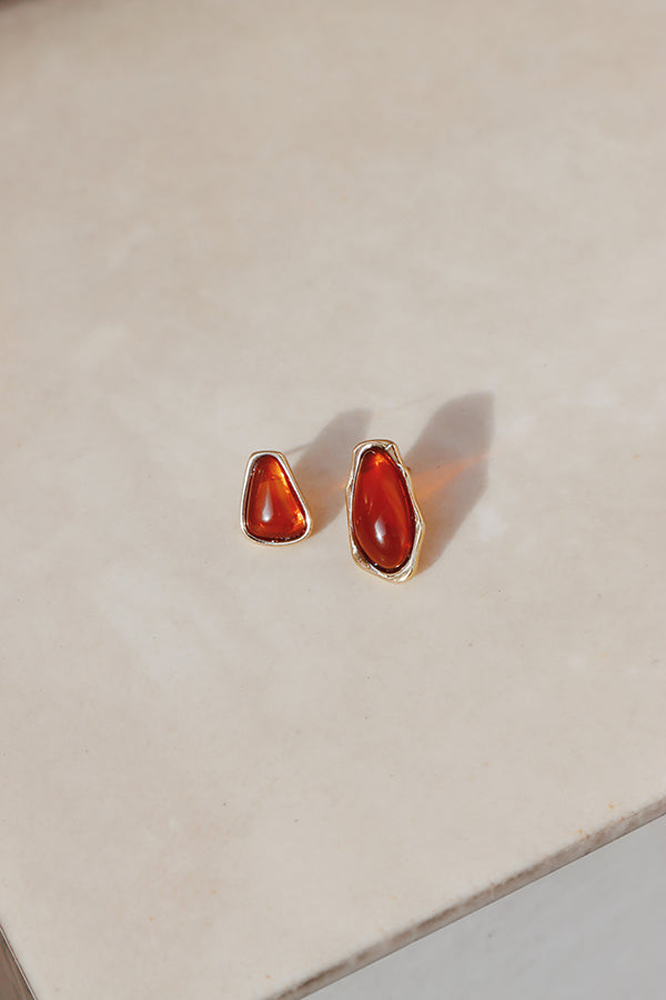 Earrings casting soft shadows under natural light, highlighting the bold red centers and artistic irregular gold outlines.