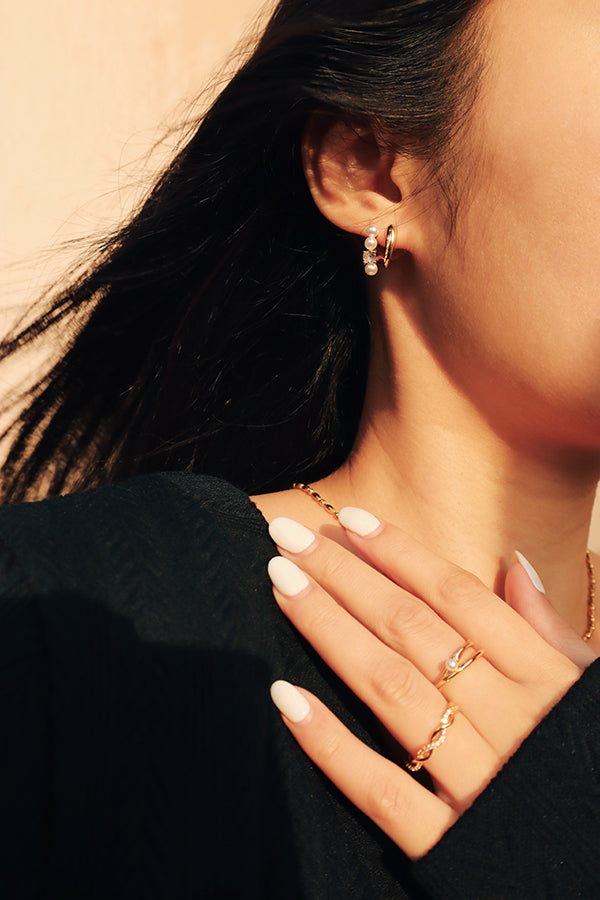 Modern and sophisticated jewelry styling with gold and pearl hoop earrings, paired with delicate rings and a chain necklace.