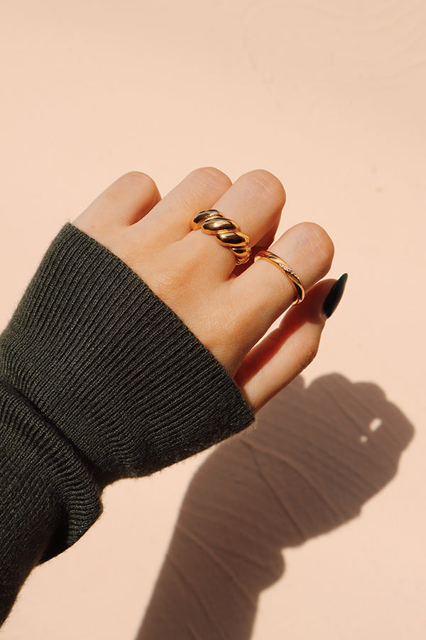 一隻手疊戴著時尚金色戒指與纖細的鋯石戒指,搭配深綠色毛衣,突顯大膽與細膩之間的平衡。