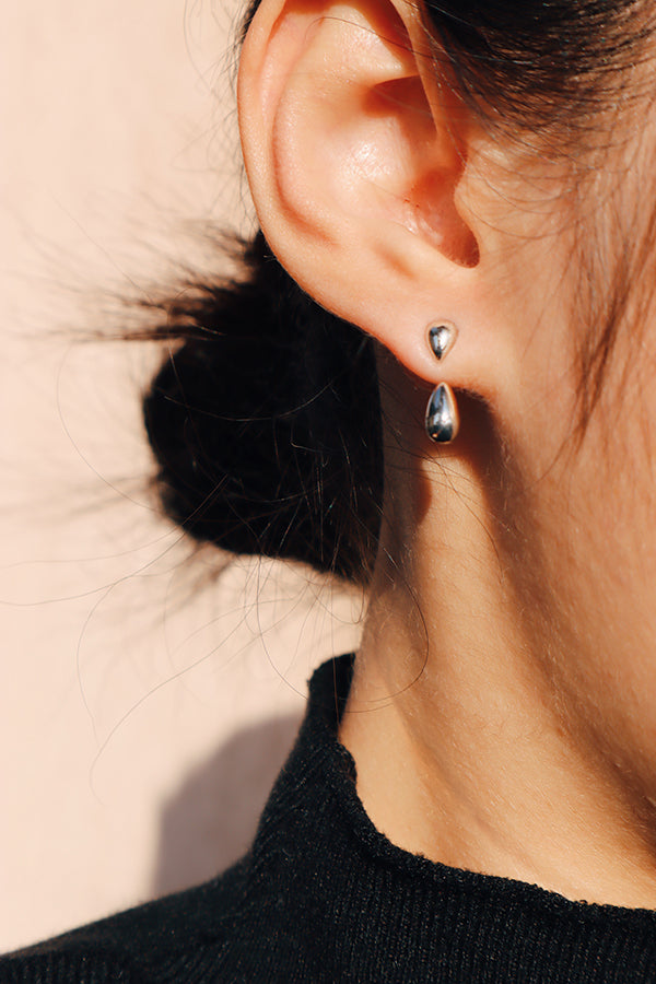 Dainty silver teardrop earrings styled on woman wearing black top, soft peach backdrop