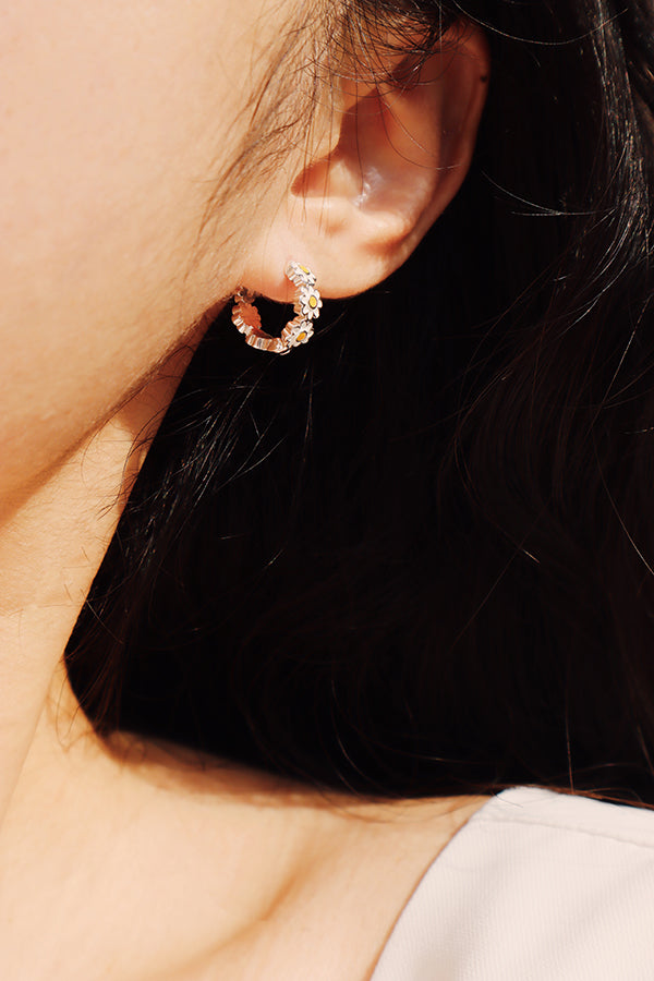 Daisy silver hoop earrings worn on ear, featuring polished petals and soft yellow centers for a fresh floral look.