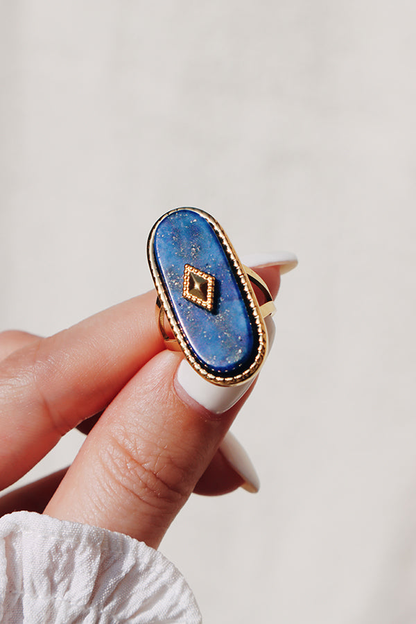 Elegant deep blue lapis lazuli ring with intricate gold accents, held between manicured fingers under natural sunlight.