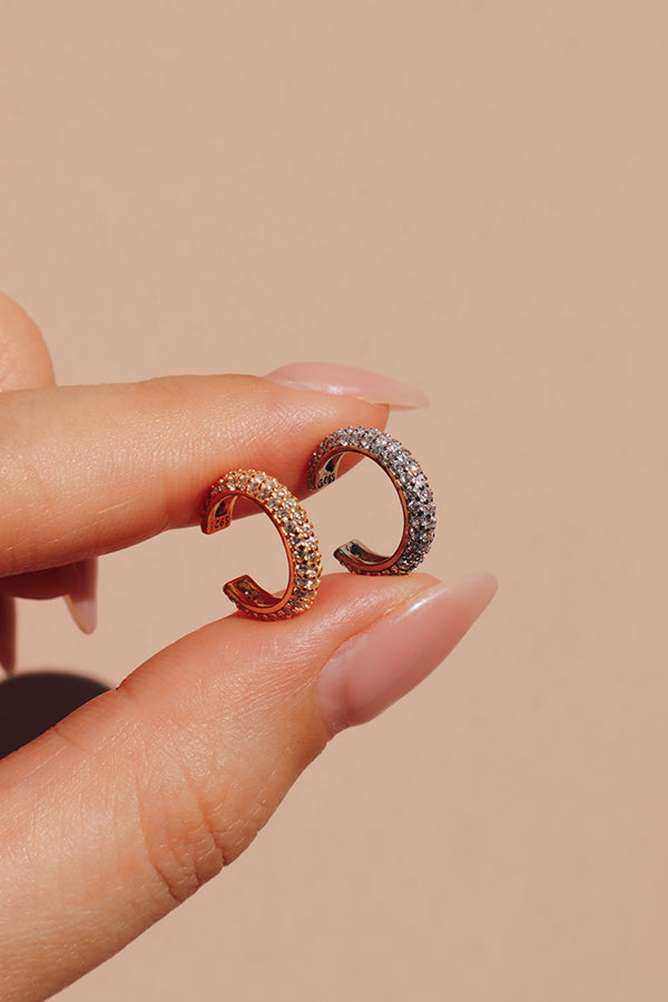 Woman holding the gold and silver shiny cz ear cuffs showing to the camera.
