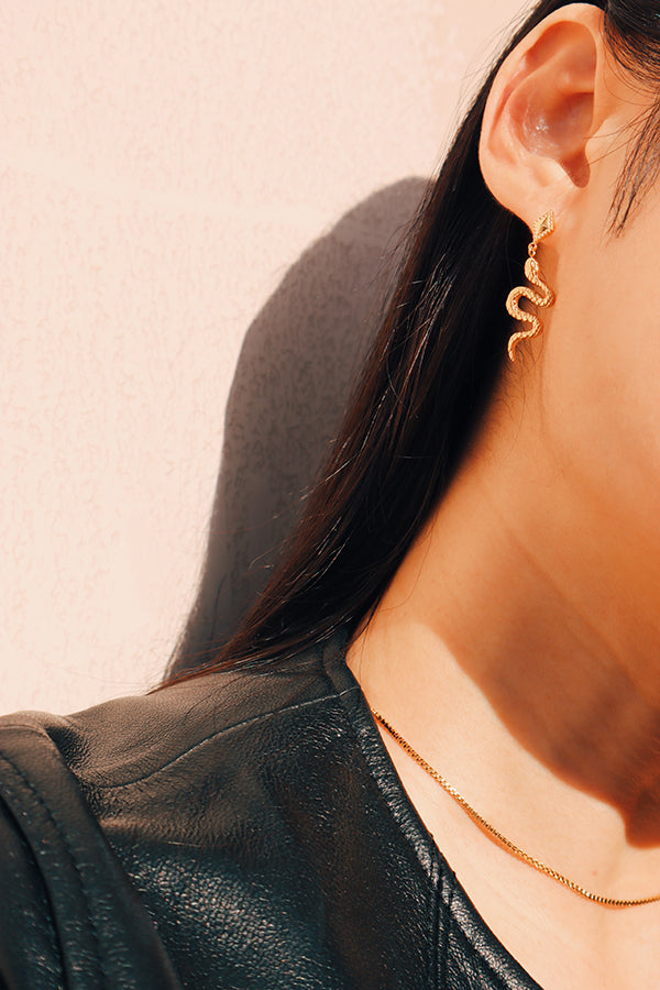 Stylish woman waering leather jacket with gold snake earrings and dainty gold necklace.