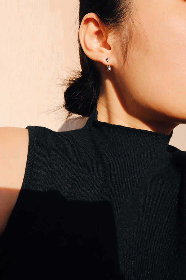 Elegant teardrop stud and drop earring stacking shown on woman with minimalist outfit