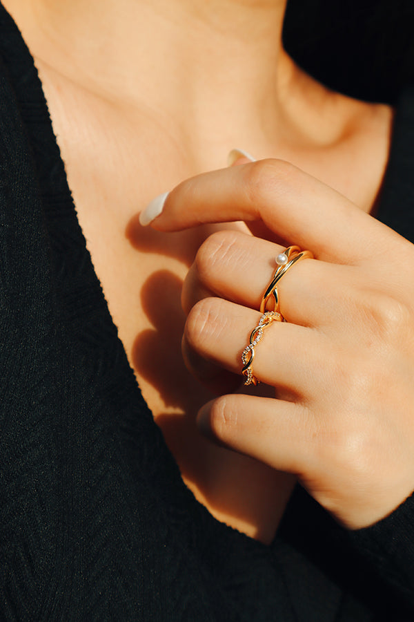 Close-up of a woman's hand wearing an elegant twisted gold ring with a delicate pearl accent, styled with a black textured outfit.