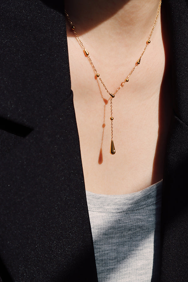 金色水滴 Y 字項鍊在光影下呈現柔和光澤,營造輕盈法式氛圍。