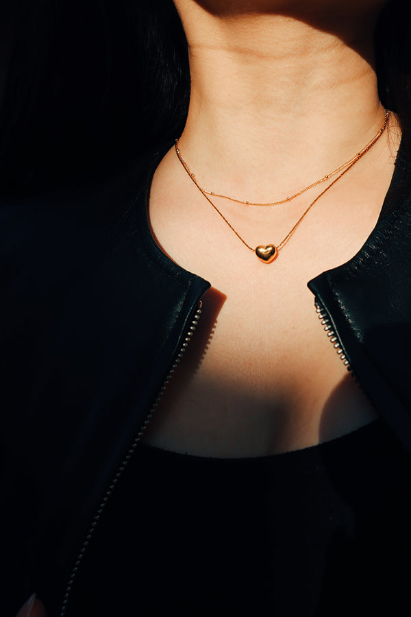 Girl in leather jacket wearing a gold heart shaped necklace layered with another slimmer necklace.