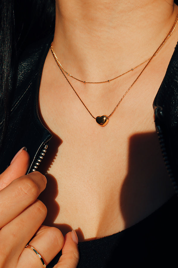 Girl in leather jacket wearing a gold heart shaped necklace layered with another slimmer necklace