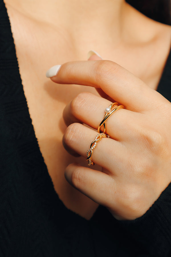 Elegant woman's hand adorned with a gold pearl ring and a twisted stackable ring, styled with a black outfit for a sophisticated and timeless look.