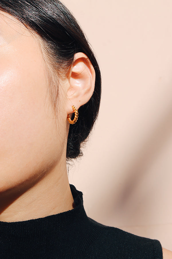 近拍一隻簡約金色扭繩耳環佩戴於耳上,搭配俐落的黑色上衣。