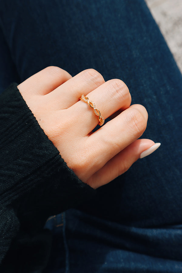 Close-up of a woman's hand wearing a delicate gold twisted ring with sparkling accents, styled with a dark sweater and denim for a casual chic look.