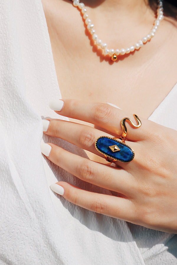 A woman's hand featuring a gold wave ring styled with a bold gemstone ring, perfect for a layered jewelry look.