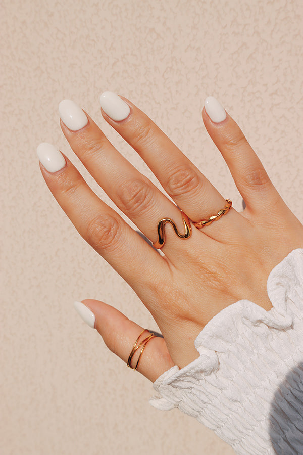 A woman's hand featuring a gold wave ring styled with a bold gemstone ring, perfect for a layered jewelry look.