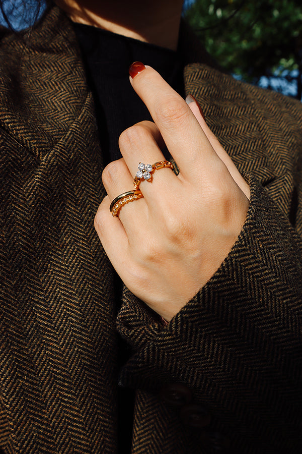 Model wearing the Liana Flora gold flower ring featuring four zircon petals and a gold bead center, styled with stacked gold rings for an elegant layered look.