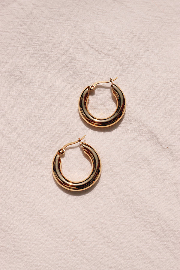 A pair of simple classic gold hoops laid down on white cloth.