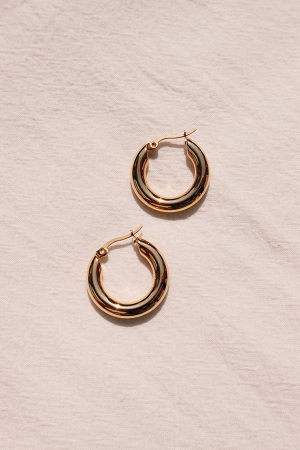 A pair of simple classic gold hoops laid down on white cloth