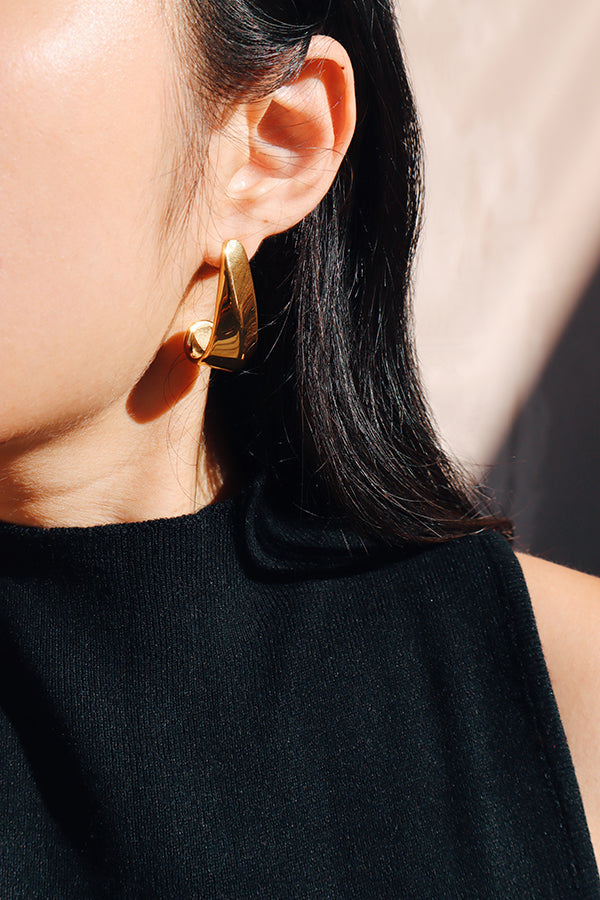 特寫鏡頭下,一位女性佩戴著時尚大膽的金色耳環,耳環設計現代且具有線條刻畫感,搭配黑色無袖上衣。