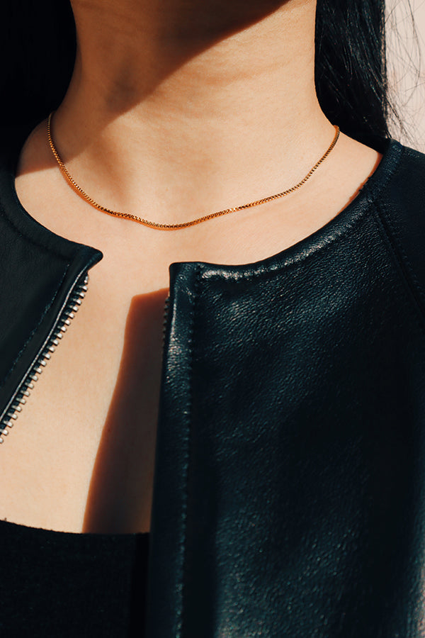 Black leather jacket girl wearing gold cube chain choker under the sun.