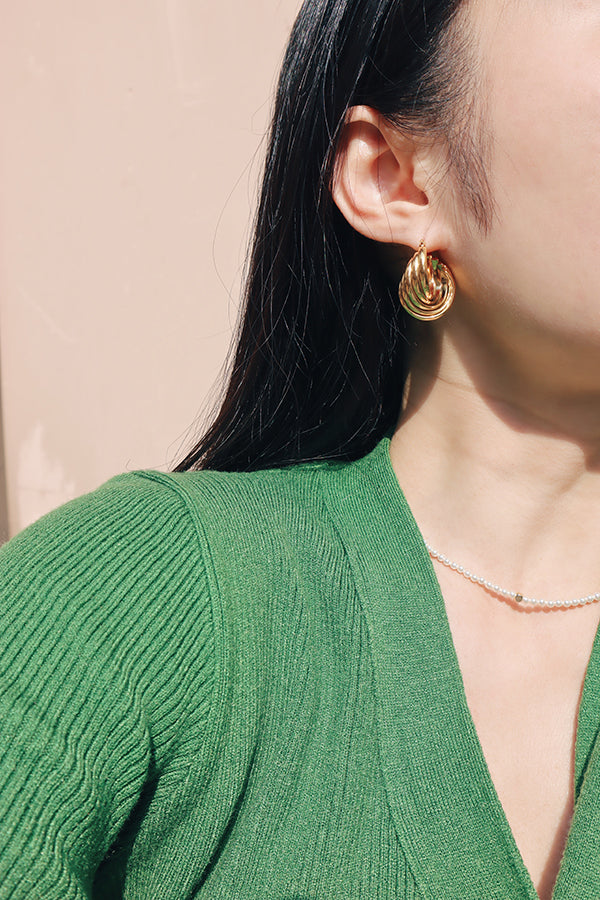 Girl wearing a green cardigan with medium size textured gold hoops along with a pearl necklace in sunlight.
