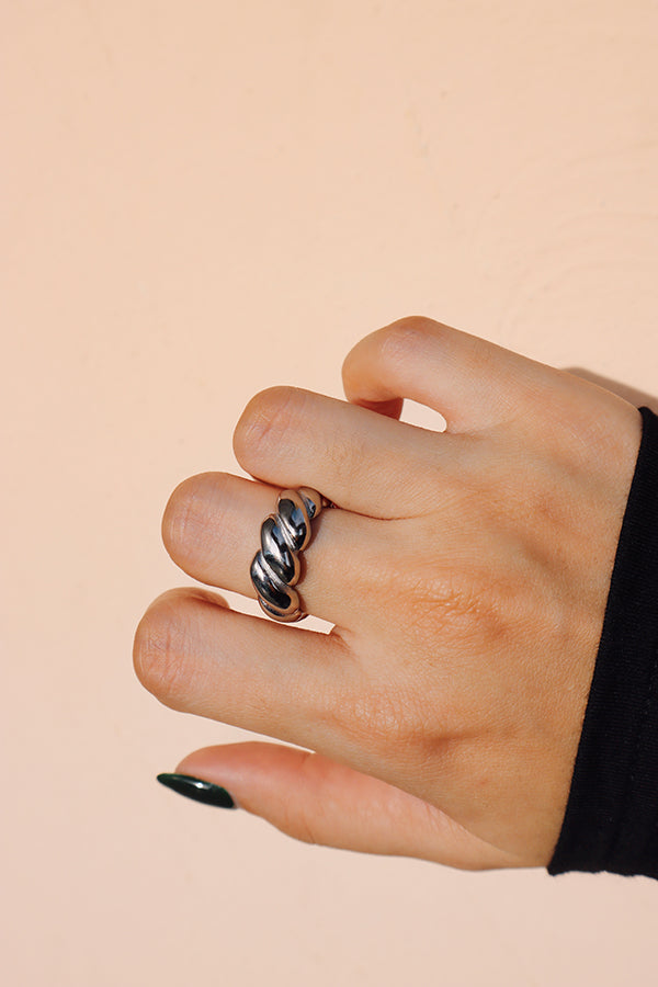 Silver croissant ring adorning a hand with forest green nails, the background in soft pastel beige highlights the rings vibrant gold color.