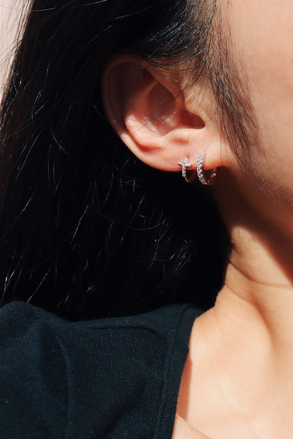 Black t-shirt girl stacking zirconia cross huggies and zirconia earring on one side under the sun.