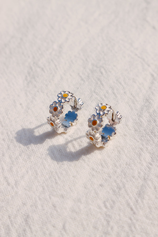 Silver daisy hoop earrings displayed flat, lightweight design with both stud and clip-on versions.