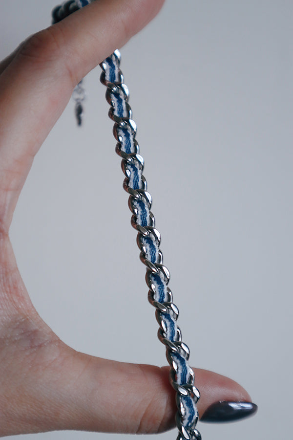 Close-up of a stainless steel chain necklace woven with blue denim fabric, highlighting its urban street style texture contrast.