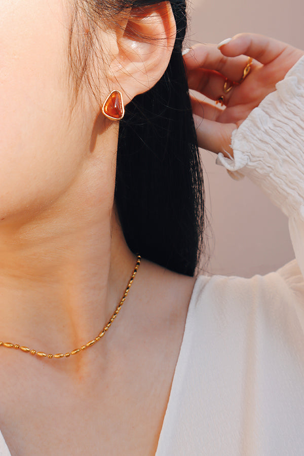 Under warm sunlight, the red and gold-framed earring glows softly, adding a striking highlight to the outfit.