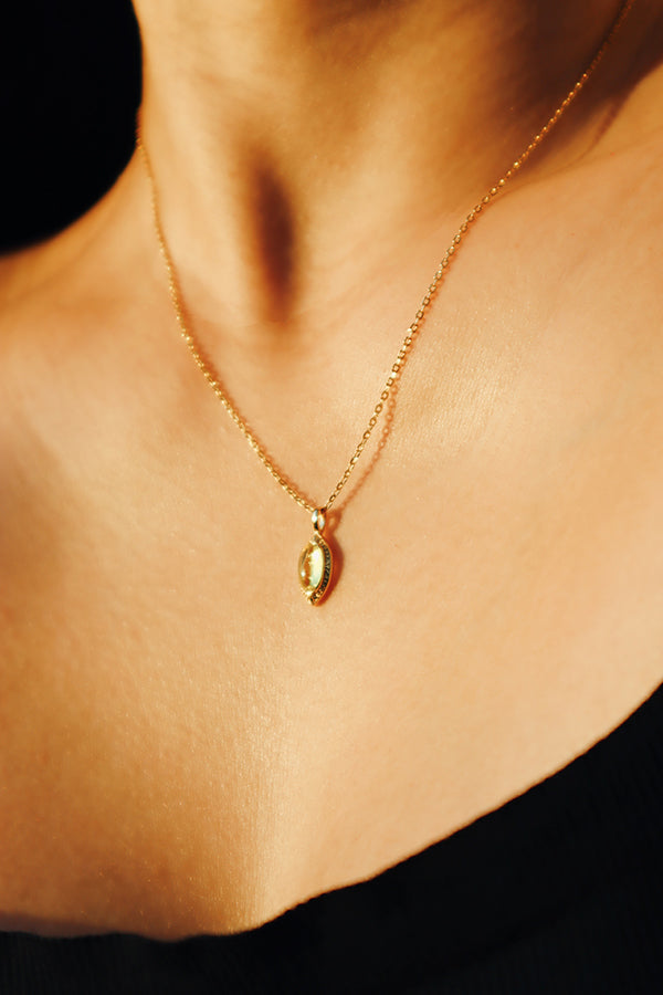 照片捕捉了女性配戴橄欖石項鍊的整體視覺效果,吊墜的黃綠色調與金色鏈條完美結合,呈現出高雅而精緻的時尚風格。