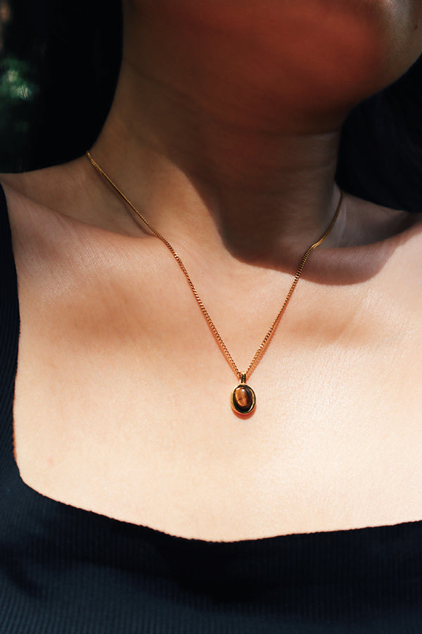 Close-up of a woman wearing a Tiger Eye pendant necklace on an 18k gold-plated chain, highlighting the gemstone's rich warm tones and the necklace's elegant simplicity.