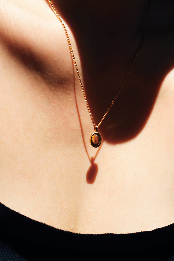 Close-up of a woman wearing a Tiger Eye pendant necklace on a gold chain, emphasizing the gemstones deep earthy tones and the necklace's timeless elegance.