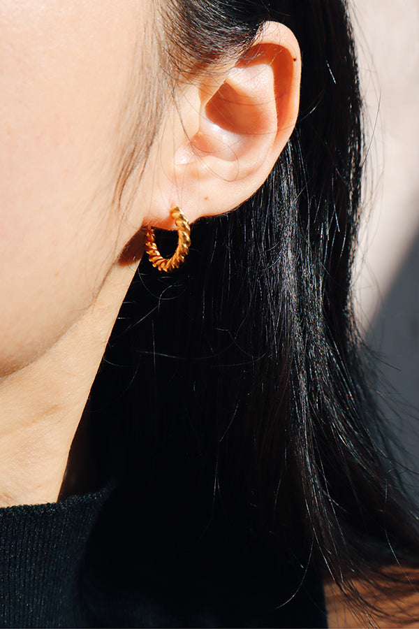 近距離拍攝一款扭紋金色小圈耳環,佩戴於女性耳朵上,呈現簡約且優雅的設計。