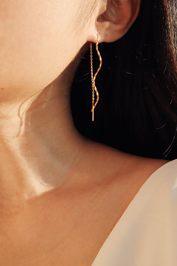 Womans ear adorned with unique threader gold earrings featuring a wavy design, emphasizing their modern and sophisticated style.