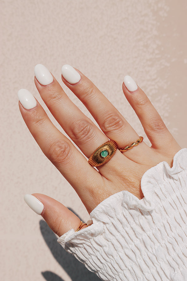 A woman wearing a vintage-inspired gold ring with a green gemstone, styled with a white textured blouse.