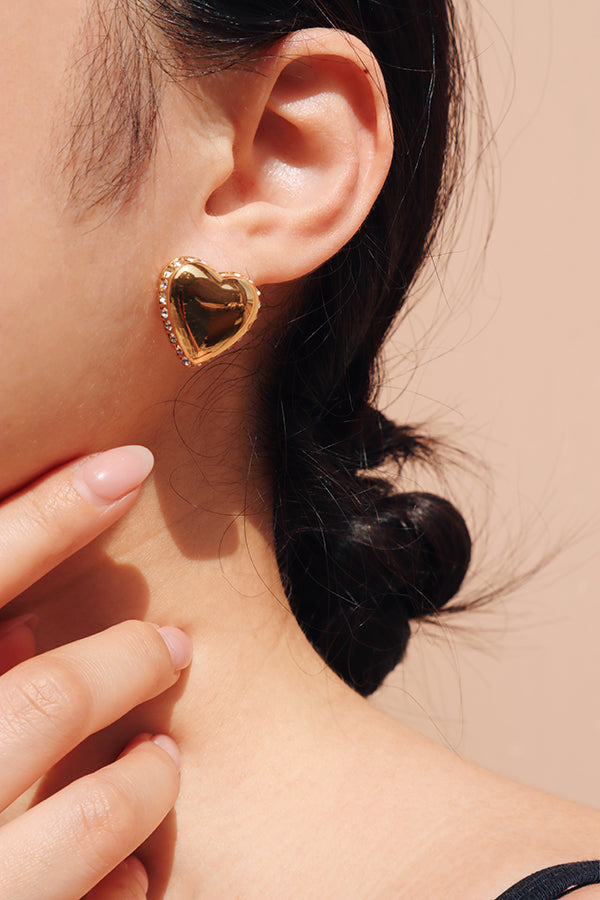 Girl directing attention to her zirconia heart shaped gold earrings with her hand under the sun