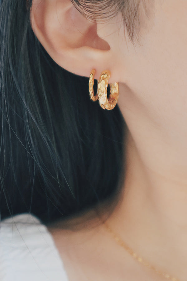 An ear wearing two gold hoop earrings: one smooth and one with a hammered texture, stacked closely.