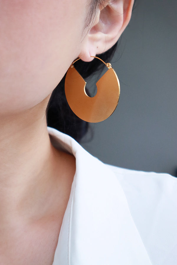 一隻耳朵佩戴著一款設計感十足的大型金色圓圈耳環,耳環呈扁平圓形,並帶有切口設計,完美展現波西米亞的藝術風格。