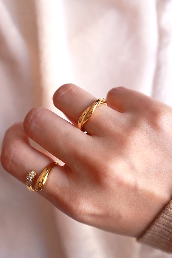 A close-up of a hand wearing a polished gold entwined or twisted band ring, suitable for daily wear.