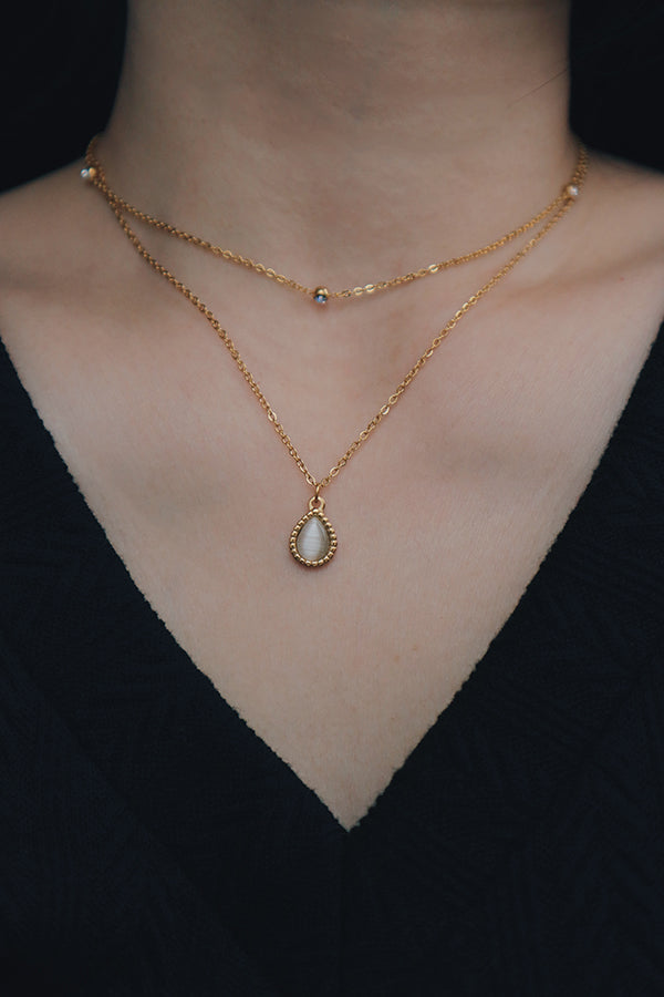 A dainty necklace featuring a teardrop-shaped pendant with a green cat's eye gemstone, worn with a white textured top, ideal for wedding outfits.