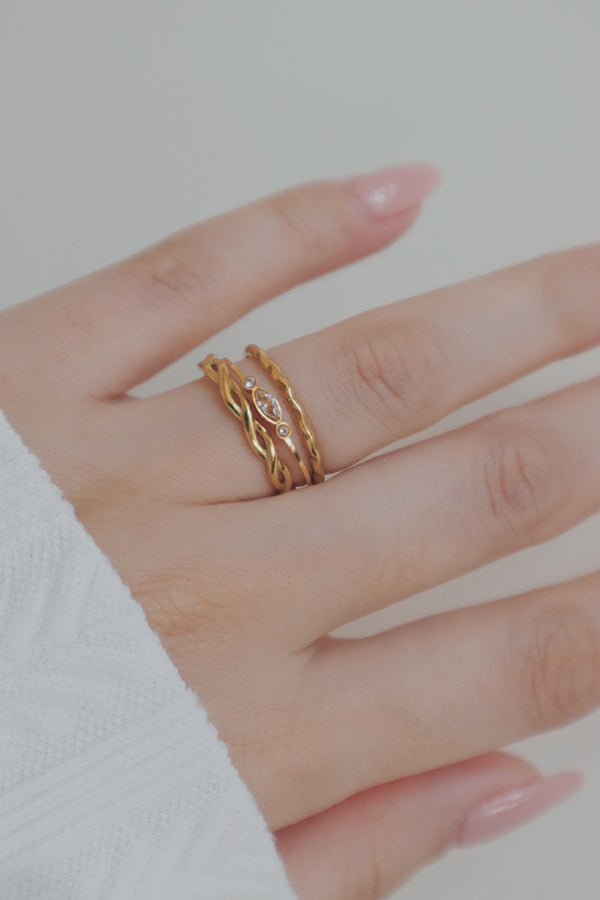 A hand wearing a single delicate gold ring with a small, elongated oval design featuring tiny clear cubic zirconia stones.
