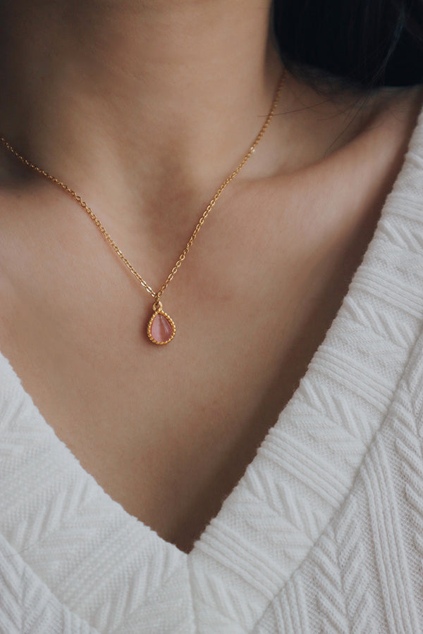 A woman wearing an elegant necklace featuring a cat's eye gemstone in a teardrop-shaped pendant, styled with a black V-neck top, showcasing its timeless design.