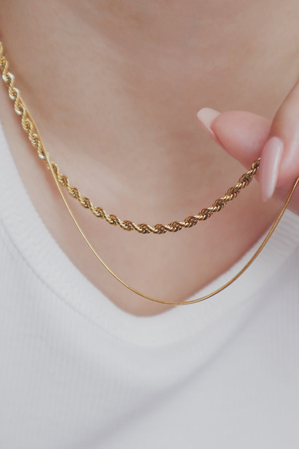 Fashionable gold stacking necklaces on a woman, each with distinct chain patterns, adding a sophisticated touch to her outfit.