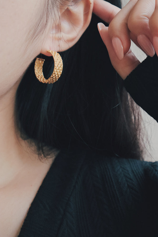 A close-up image of a woman's ear adorned with textured gold hoop earrings. The earrings are designed with a bold, patterned texture that adds a touch of elegance and sophistication to everyday wear.
