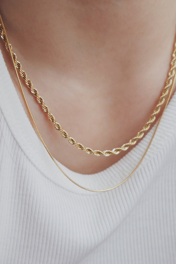 Close-up of a womans neckline adorned with three elegant gold layering necklaces in different styles for a chic look.