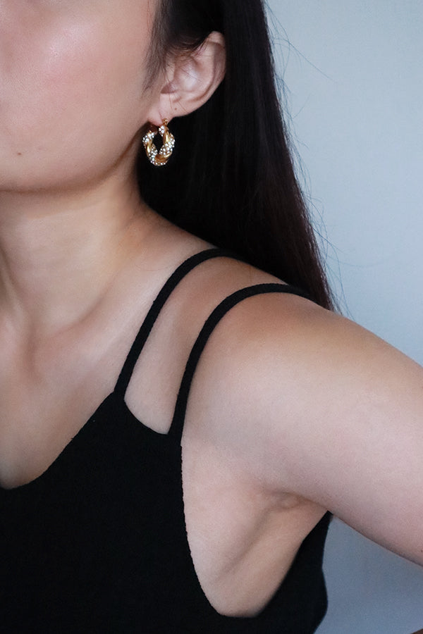 A woman's ear wearing a trendy gold twisted hoop earring, accented with sparkling stones, styled as a statement piece.