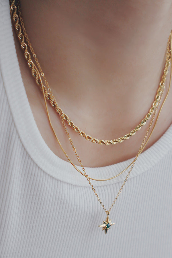 A person wearing a set of three layered gold chain necklaces, including a rope chain, a delicate smooth chain, and a fine chain with a small star pendant.